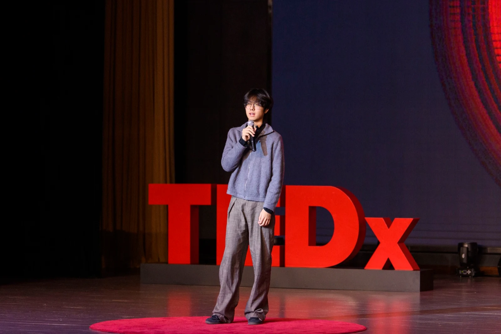 Rayn Lee speaking on the TEDxOTIA Youth stage in front of the TEDx letters